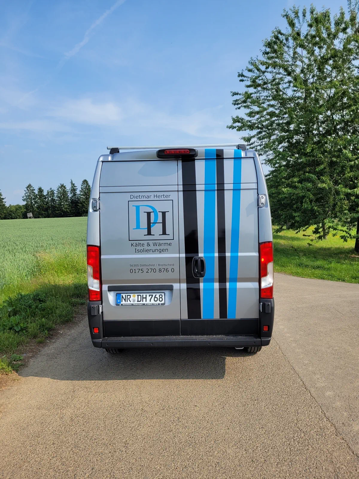 Fahrzeugbeschriftung: Silberner Transporter mit blauen & schwarzen Streifen, Firmenlogo 'Dietmar Herter'. Professionelle Folierung.