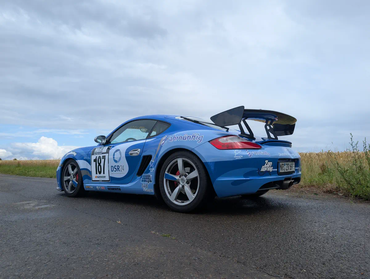 Blauer Porsche Cayman mit auffälliger Rennfolierung und Sponsorenlogos, ideal für Event-Branding und professionelle Fahrzeugbeschriftung.