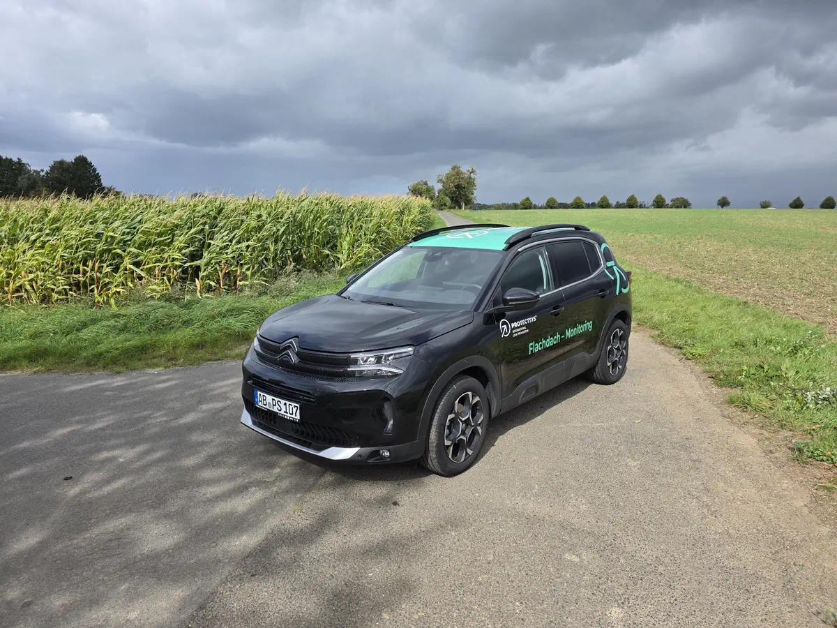 Schwarzer Citroen mit auffälliger Flottenbeschriftung für Flachdach-Monitoring im Außeneinsatz. Professionelle Fahrzeugfolierung.