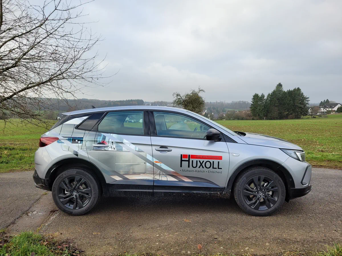 Professionelle Fahrzeugbeschriftung: Silberner PKW mit HUXOLL-Logo und Grafik. Effektives Car Wrapping für mobile Werbung.