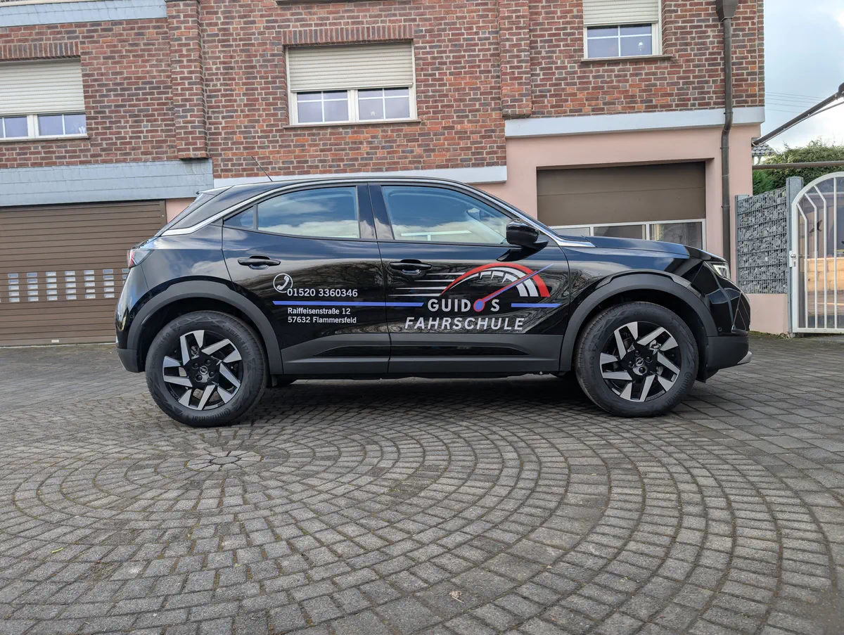 Professionelle Fahrzeugbeschriftung: Schwarzer Opel Mokka mit auffälliger Werbung für Guido's Fahrschule. Werbetechnik vom Fachmann.